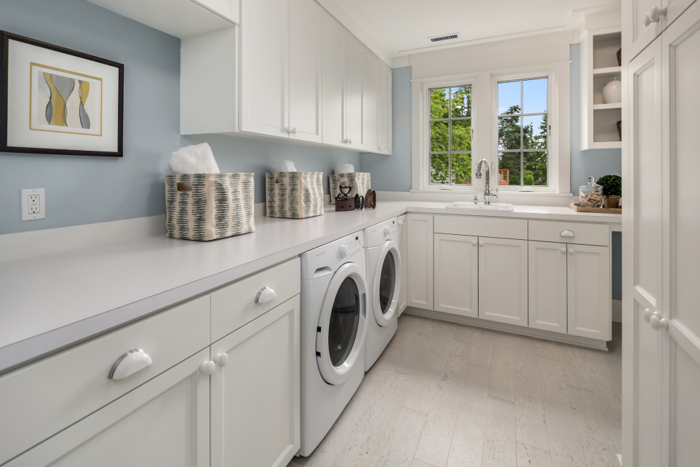 シアトルにある広いトランジショナルスタイルのおしゃれな洗濯室 (L型、ドロップインシンク、シェーカースタイル扉のキャビネット、白いキャビネット、青い壁、磁器タイルの床、左右配置の洗濯機・乾燥機、ベージュの床、白いキッチンカウンター) の写真