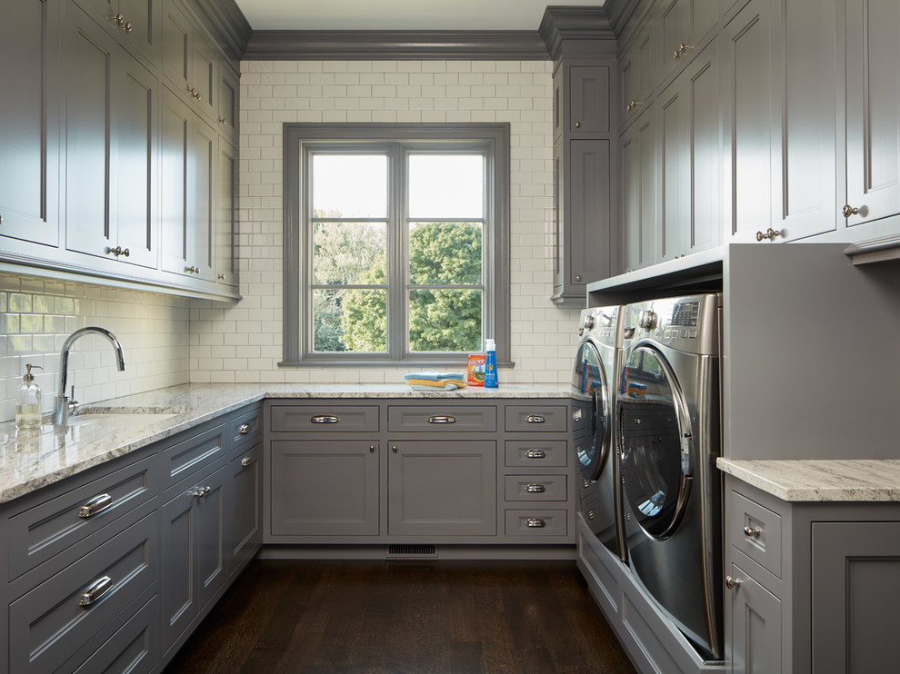Exempel på en klassisk tvättstuga enbart för tvätt, med grå skåp, bänkskiva i kvartsit, mörkt trägolv och en tvättmaskin och torktumlare bredvid varandra