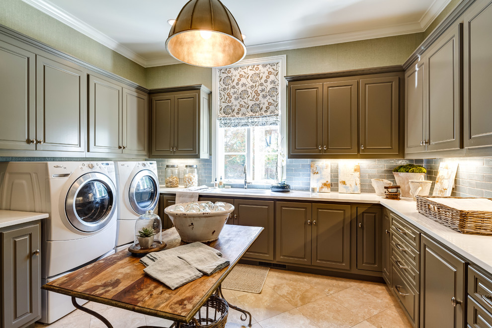 Große Klassische Waschküche in L-Form mit profilierten Schrankfronten, grüner Wandfarbe, Travertin, Waschmaschine und Trockner nebeneinander und braunen Schränken in Atlanta