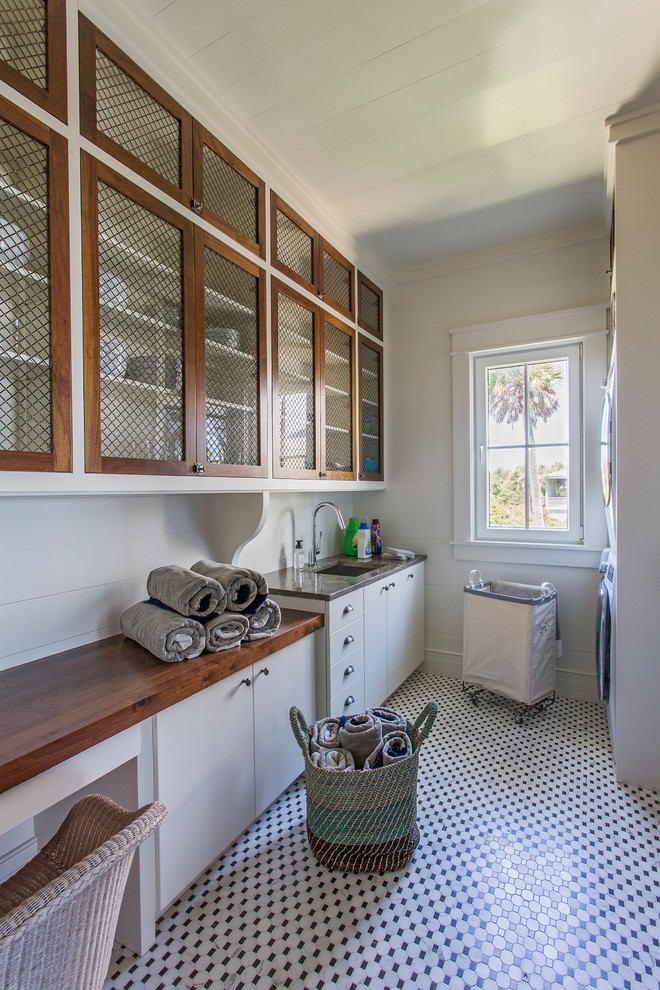 Inspiration for a large tropical galley dedicated laundry room remodel in Charleston with an undermount sink, white cabinets, wood countertops, white walls, a stacked washer/dryer and brown countertops