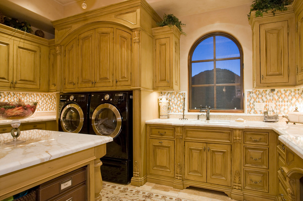 Geräumige Mediterrane Waschküche in U-Form mit Einbauwaschbecken, profilierten Schrankfronten, hellbraunen Holzschränken, Granit-Arbeitsplatte, beiger Wandfarbe, Travertin und Waschmaschine und Trockner nebeneinander in Phoenix