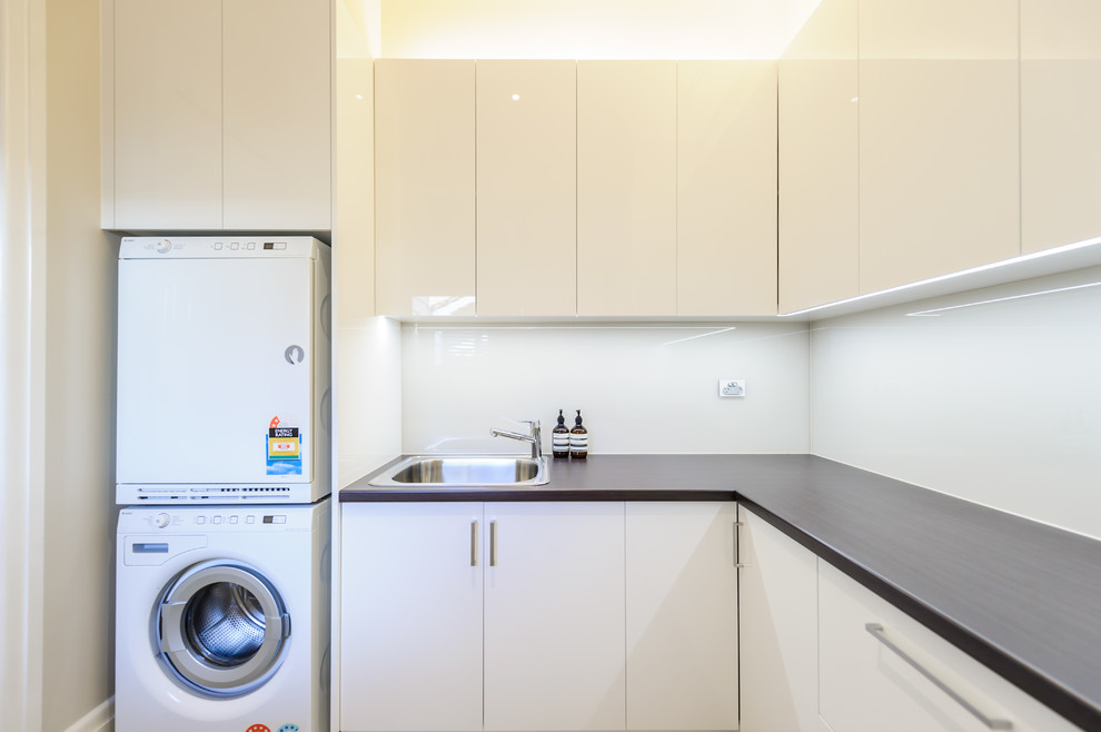 This is an example of a medium sized contemporary l-shaped separated utility room in Melbourne with a built-in sink, flat-panel cabinets, laminate countertops, concrete flooring, a stacked washer and dryer and white cabinets.