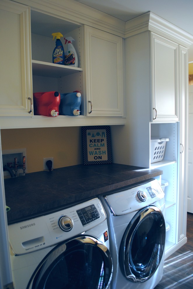 Foto di una sala lavanderia classica di medie dimensioni con ante con bugna sagomata, ante bianche, top in laminato, pareti gialle, pavimento in laminato e lavatrice e asciugatrice affiancate