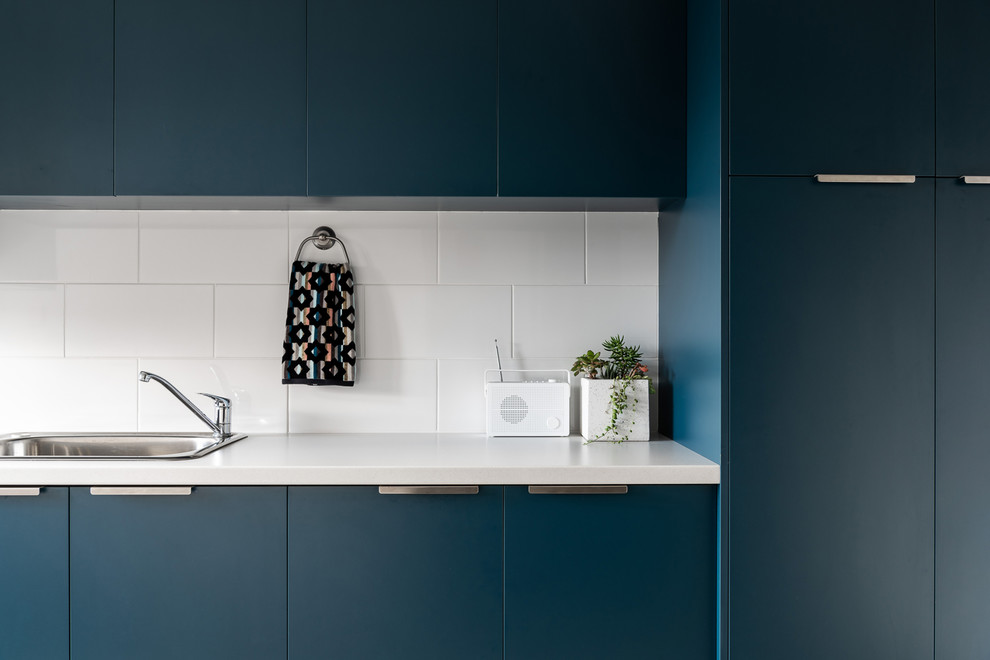 Esempio di una grande lavanderia moderna con lavello a vasca singola, ante blu, pareti bianche, pavimento con piastrelle in ceramica, lavatrice e asciugatrice a colonna, pavimento grigio e top bianco