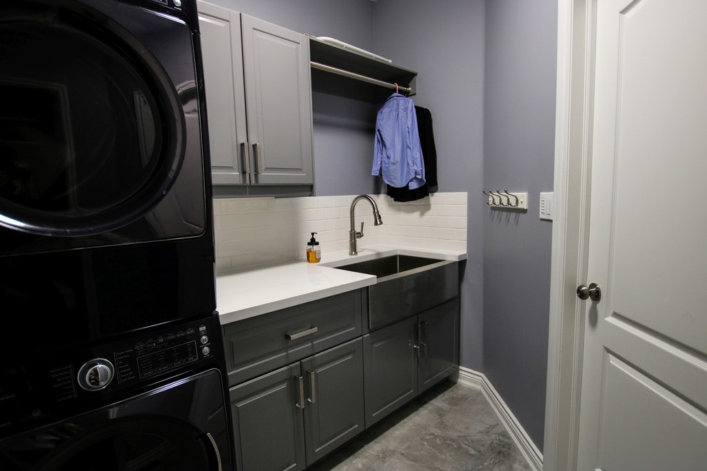 Small traditional single-wall separated utility room in Toronto with a belfast sink, shaker cabinets, grey cabinets, engineered stone countertops, grey walls, porcelain flooring, a stacked washer and dryer and grey floors.