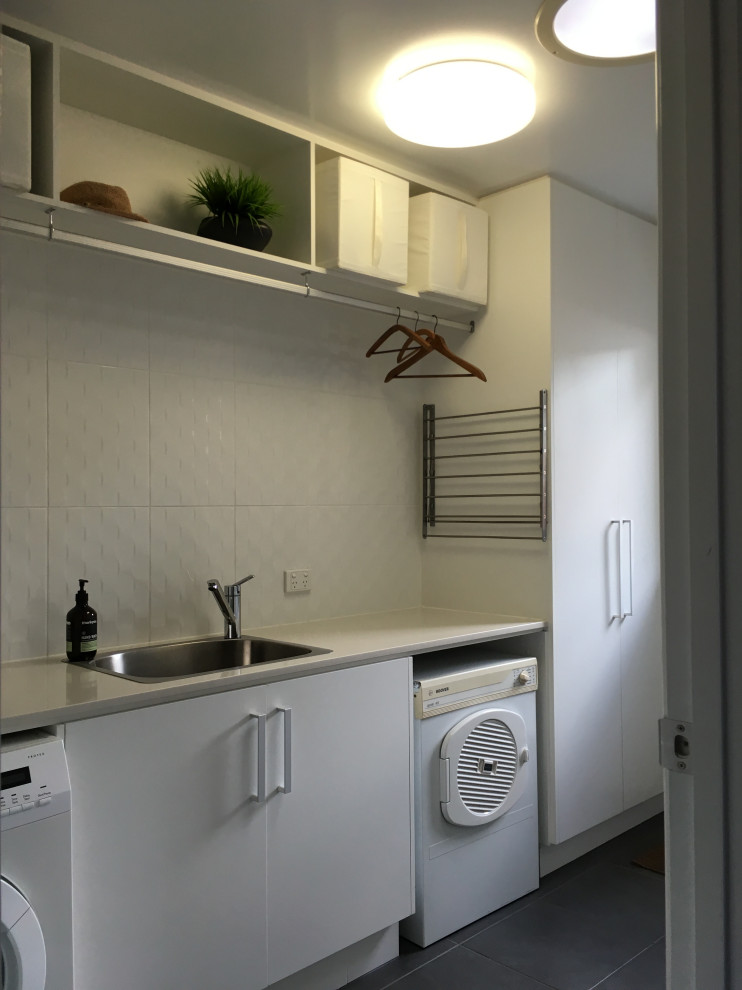 Esempio di una sala lavanderia minimalista di medie dimensioni con lavello da incasso, ante lisce, top in superficie solida, pareti bianche, pavimento in gres porcellanato, pavimento grigio e top beige