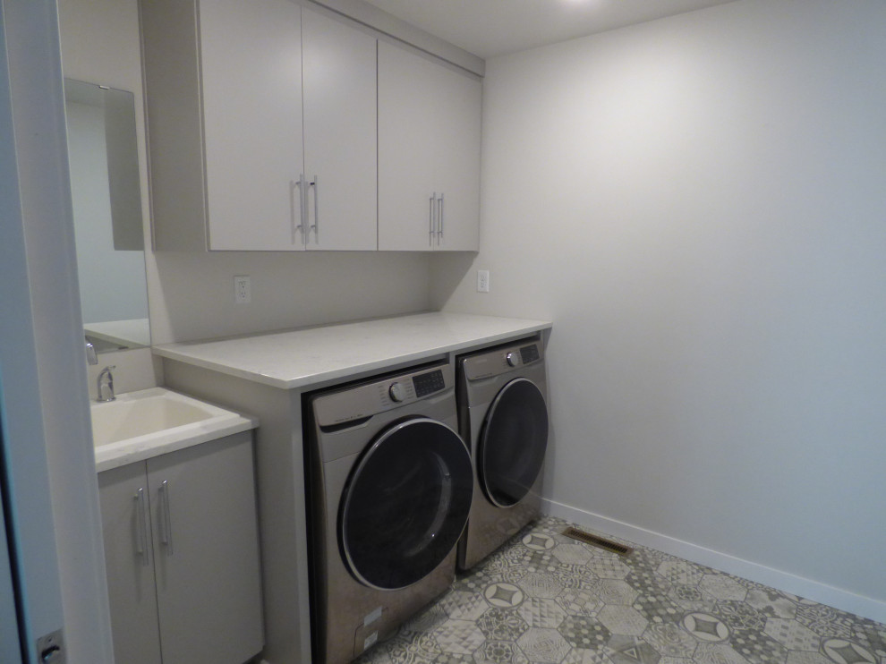 Esempio di una sala lavanderia contemporanea di medie dimensioni con lavatoio, ante grigie, top in granito, pareti bianche, pavimento in vinile, lavasciuga, pavimento grigio e top bianco