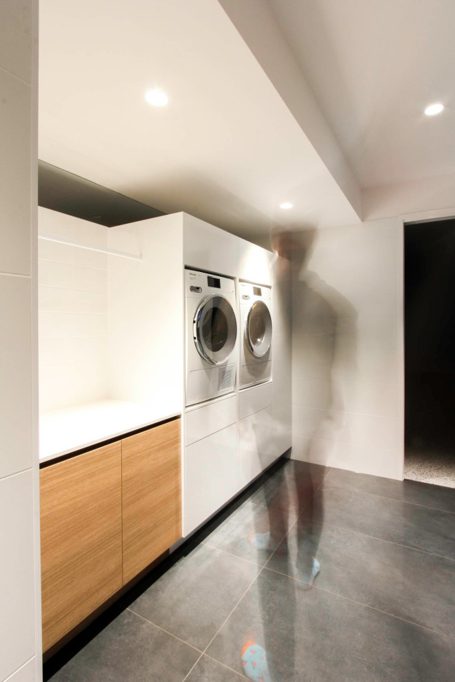 Exempel på en stor modern vita parallell vitt tvättstuga enbart för tvätt, med skåp i ljust trä, marmorbänkskiva, vita väggar, klinkergolv i keramik, en tvättmaskin och torktumlare bredvid varandra och grått golv