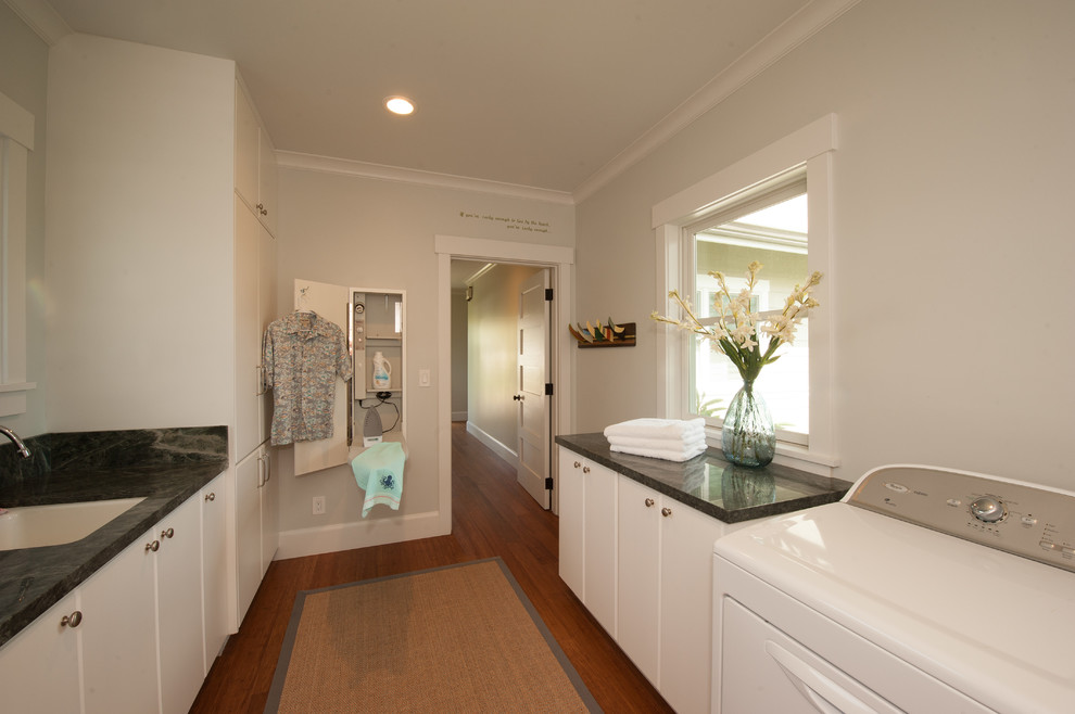 Diseño de cuarto de lavado de estilo americano con puertas de armario blancas, encimera de granito, suelo de bambú y lavadora y secadora juntas