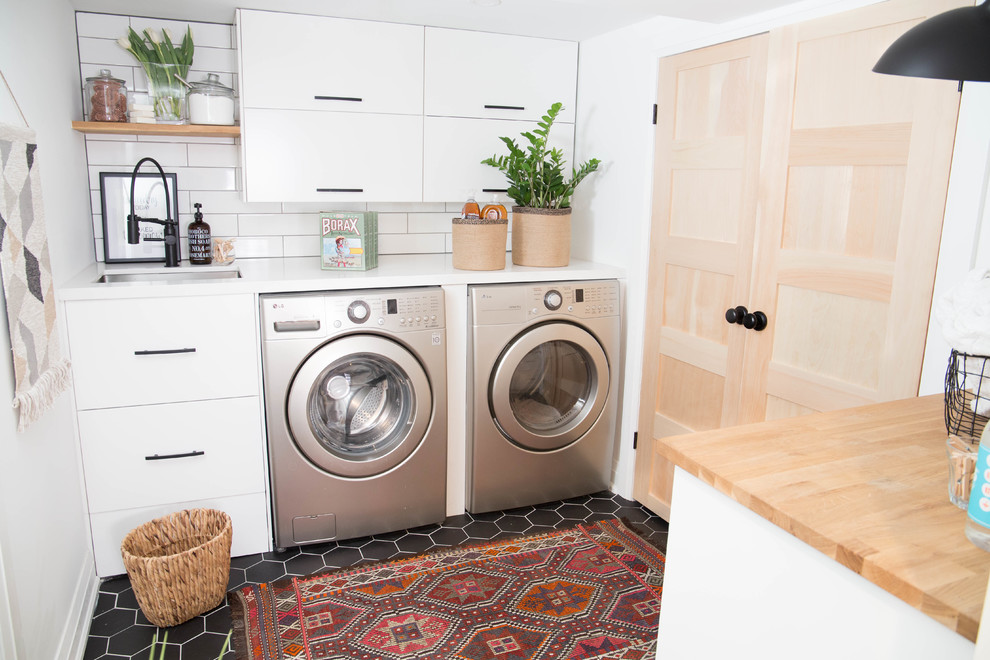 Kleine Moderne Waschküche mit Unterbauwaschbecken, flächenbündigen Schrankfronten, weißen Schränken, Quarzwerkstein-Arbeitsplatte, weißer Wandfarbe, Keramikboden, Waschmaschine und Trockner nebeneinander und schwarzem Boden in Toronto