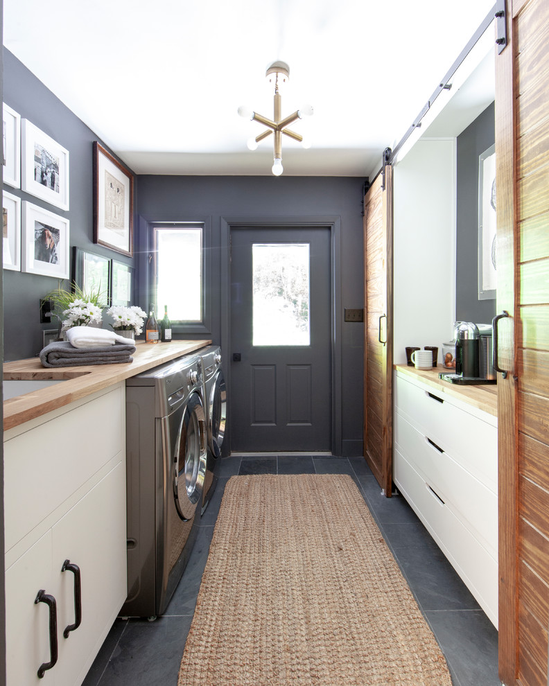 Inspiration for a country gray floor and slate floor laundry room remodel in Charlotte with an undermount sink, flat-panel cabinets, wood countertops, gray walls, a side-by-side washer/dryer, beige countertops and white cabinets
