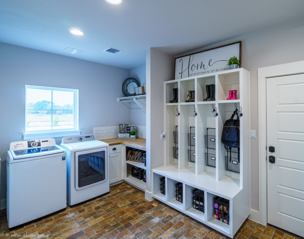 This is an example of a large rural u-shaped utility room in Austin with a belfast sink, recessed-panel cabinets, white cabinets, wood worktops, grey walls, porcelain flooring, a side by side washer and dryer and multi-coloured floors.