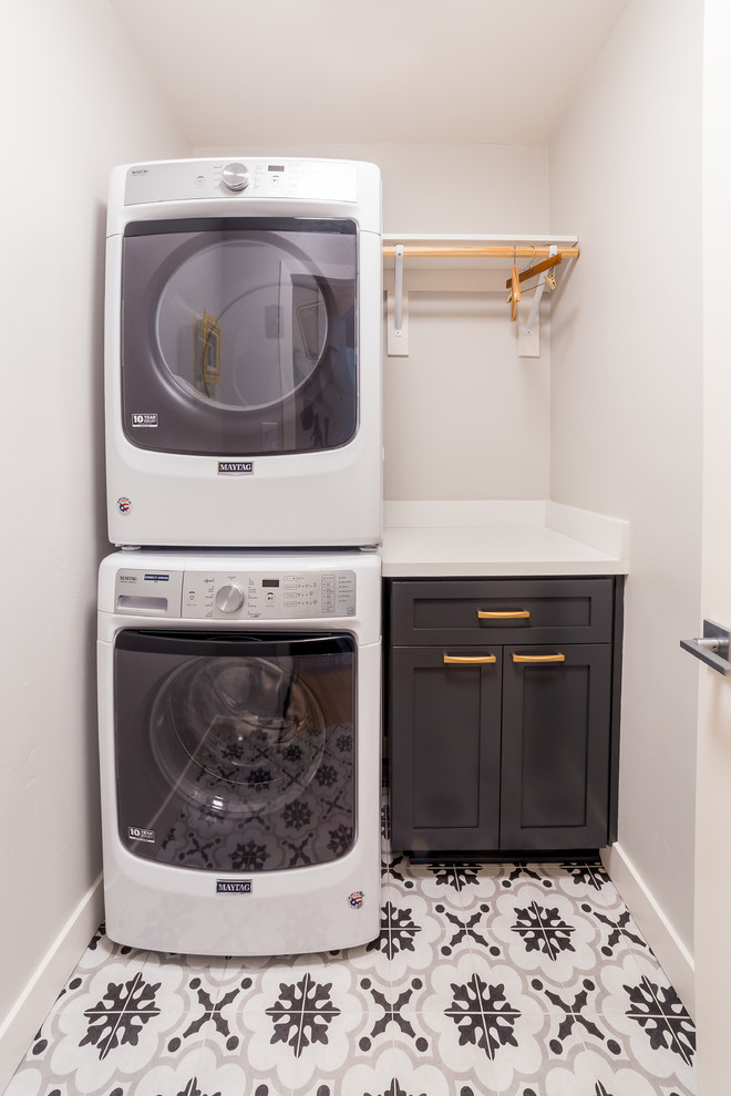 Inspiration for a mid-sized mid-century modern single-wall ceramic tile and multicolored floor dedicated laundry room remodel in San Diego with raised-panel cabinets, dark wood cabinets, granite countertops, white walls, a stacked washer/dryer and white countertops