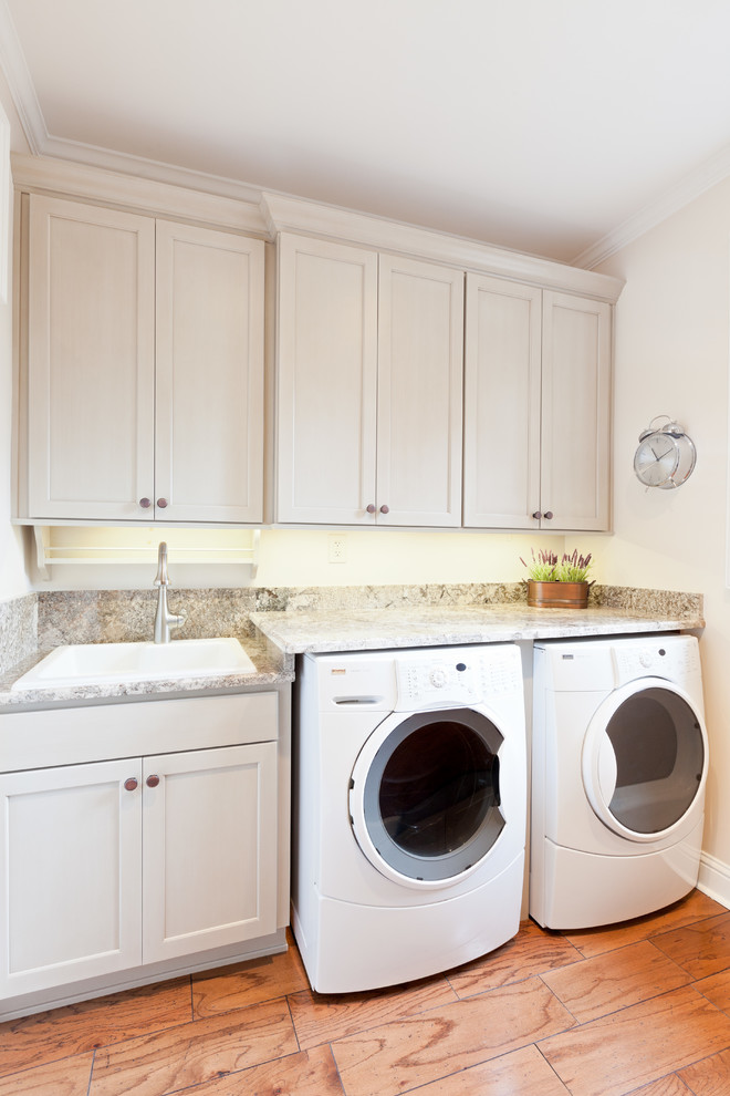 Idéer för mellanstora vintage parallella flerfärgat tvättstugor enbart för tvätt, med en nedsänkt diskho, luckor med infälld panel, beige skåp, granitbänkskiva, vita väggar, mellanmörkt trägolv, en tvättmaskin och torktumlare bredvid varandra och brunt golv
