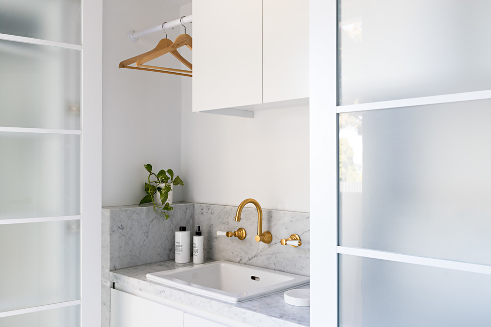 Small modern galley separated utility room in Melbourne with a built-in sink, flat-panel cabinets, white cabinets, marble worktops, white walls, porcelain flooring, a side by side washer and dryer, beige floors and white worktops.