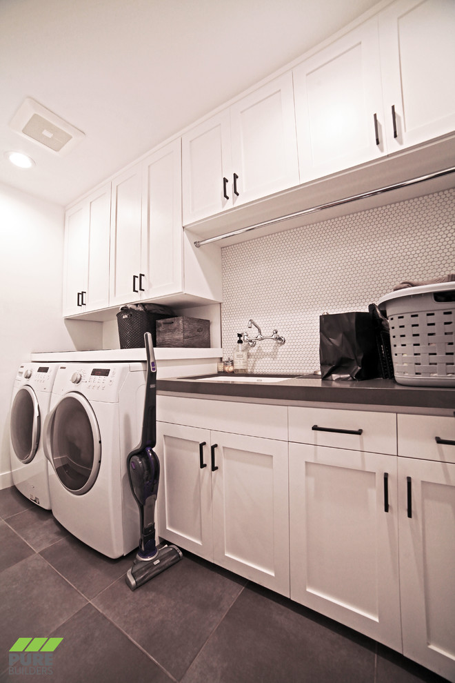 Example of a mid-sized trendy single-wall slate floor and gray floor dedicated laundry room design in Los Angeles with an undermount sink, shaker cabinets, white cabinets, solid surface countertops, white walls, a side-by-side washer/dryer and gray countertops