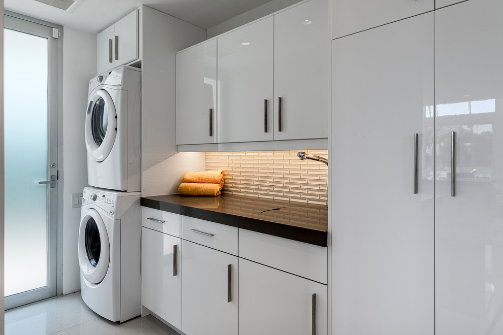 Photo of a large contemporary single-wall utility room in Los Angeles with a submerged sink, flat-panel cabinets, white cabinets, quartz worktops, white walls and a stacked washer and dryer.