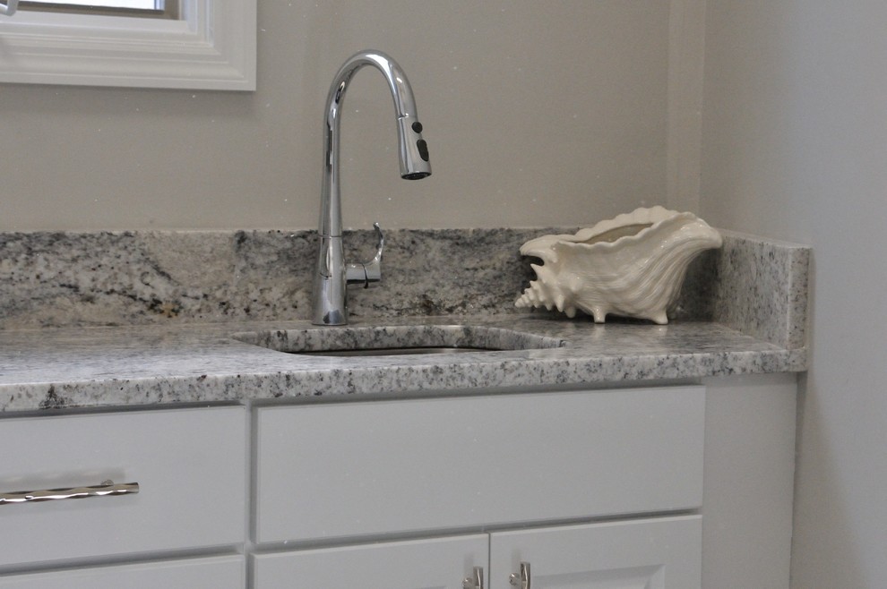 Exempel på en liten klassisk grå linjär grått liten tvättstuga, med luckor med upphöjd panel, gula skåp, granitbänkskiva, grå väggar, mellanmörkt trägolv, en tvättmaskin och torktumlare bredvid varandra och brunt golv