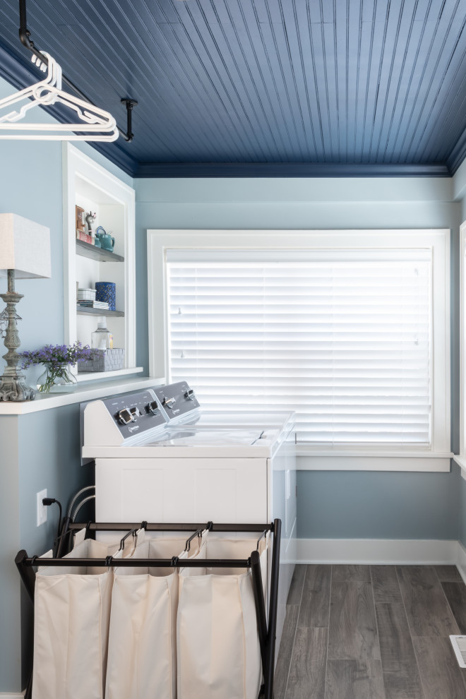 Cette photo montre une buanderie linéaire chic multi-usage avec un mur bleu, un sol en carrelage de porcelaine, des machines côte à côte, un sol marron, un plafond en bois et du lambris.