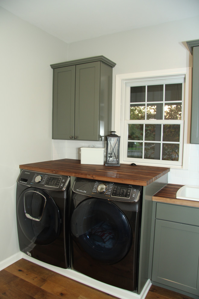 Design ideas for a small farmhouse single-wall utility room in Indianapolis with a built-in sink, shaker cabinets, green cabinets, wood worktops, grey walls, medium hardwood flooring, a side by side washer and dryer, brown floors and brown worktops.
