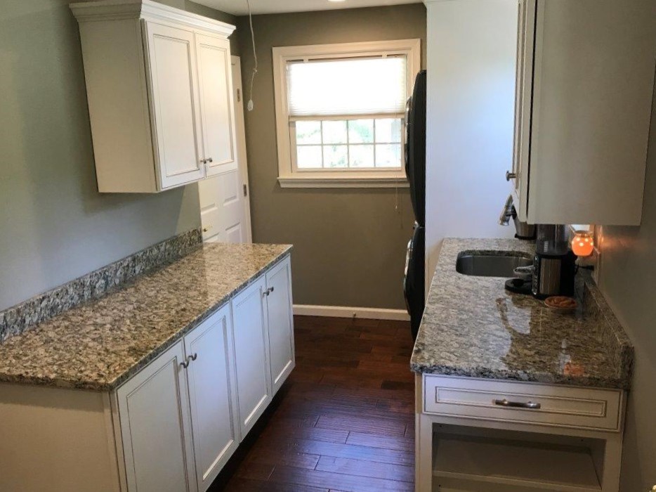 This is an example of a large traditional galley utility room in Philadelphia with a submerged sink, flat-panel cabinets, white cabinets, granite worktops, green walls, dark hardwood flooring, a stacked washer and dryer and brown floors.