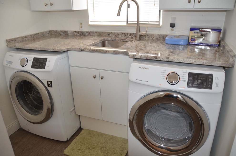 Exempel på en liten modern linjär tvättstuga enbart för tvätt, med en undermonterad diskho, släta luckor, vita skåp, granitbänkskiva, plywoodgolv och en tvättmaskin och torktumlare bredvid varandra