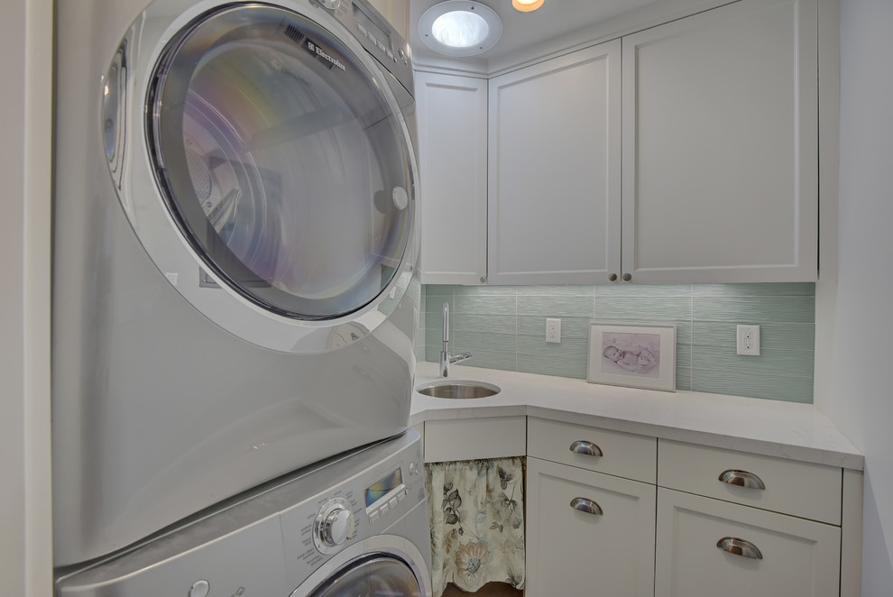 Small trendy u-shaped ceramic tile dedicated laundry room photo in San Francisco with a single-bowl sink, recessed-panel cabinets, white cabinets, solid surface countertops, green walls and a stacked washer/dryer