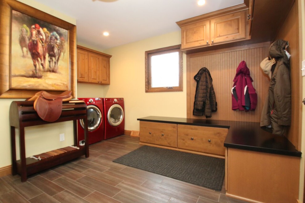 Immagine di una grande lavanderia multiuso chic con ante con bugna sagomata, ante in legno scuro, top in legno, pareti gialle, pavimento in gres porcellanato e lavatrice e asciugatrice affiancate