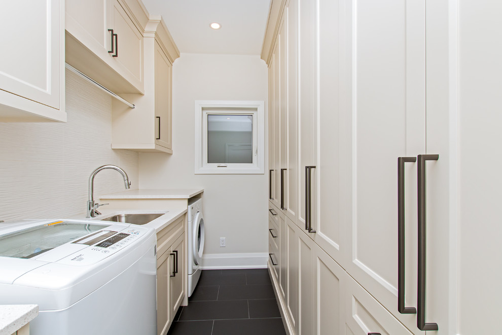 Dedicated laundry room - mid-sized traditional galley porcelain tile and black floor dedicated laundry room idea in Toronto with an undermount sink, recessed-panel cabinets, beige cabinets, beige walls, a side-by-side washer/dryer and beige countertops