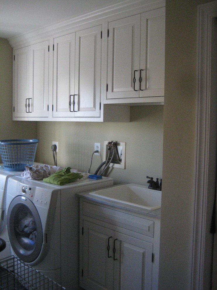 Diseño de cuarto de lavado lineal tradicional renovado de tamaño medio con fregadero encastrado, armarios con paneles con relieve, puertas de armario blancas, encimera de acrílico, paredes beige y lavadora y secadora juntas
