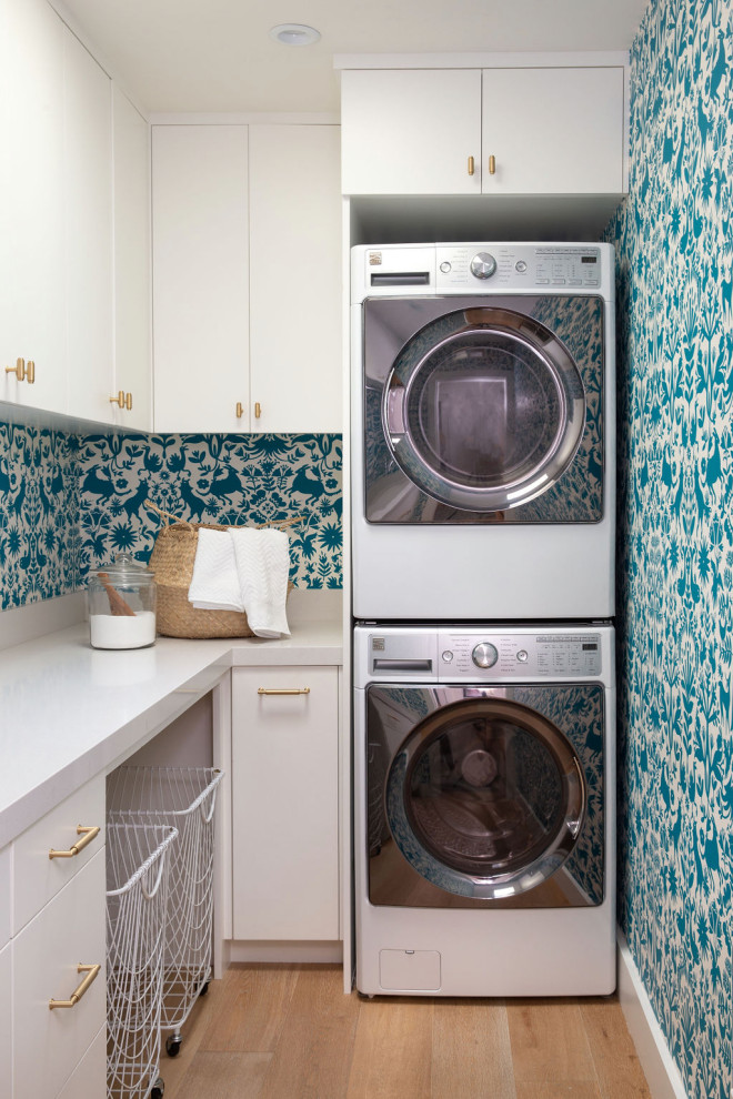 Inspiration for an eclectic l-shaped utility room in Santa Barbara with flat-panel cabinets, white cabinets, blue walls, light hardwood flooring, a side by side washer and dryer, beige floors and white worktops.