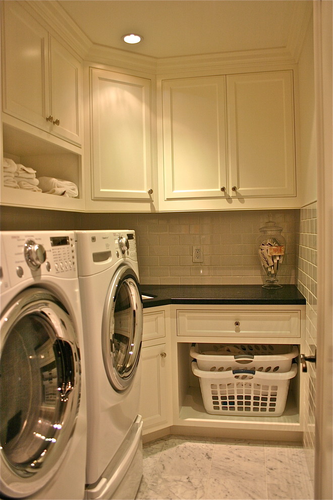 Exempel på en liten amerikansk l-formad tvättstuga enbart för tvätt, med en undermonterad diskho, vita skåp, granitbänkskiva, marmorgolv, en tvättmaskin och torktumlare bredvid varandra, luckor med infälld panel och grått golv