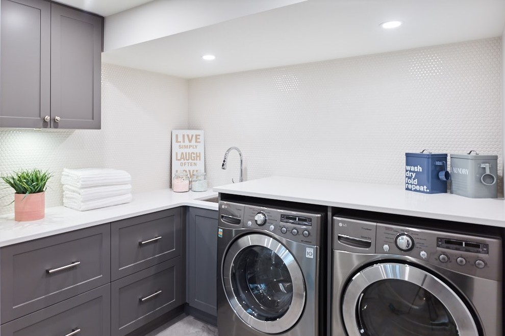 Foto på en mellanstor funkis vita l-formad tvättstuga enbart för tvätt, med en undermonterad diskho, skåp i shakerstil, grå skåp, vita väggar, en tvättmaskin och torktumlare bredvid varandra och grått golv