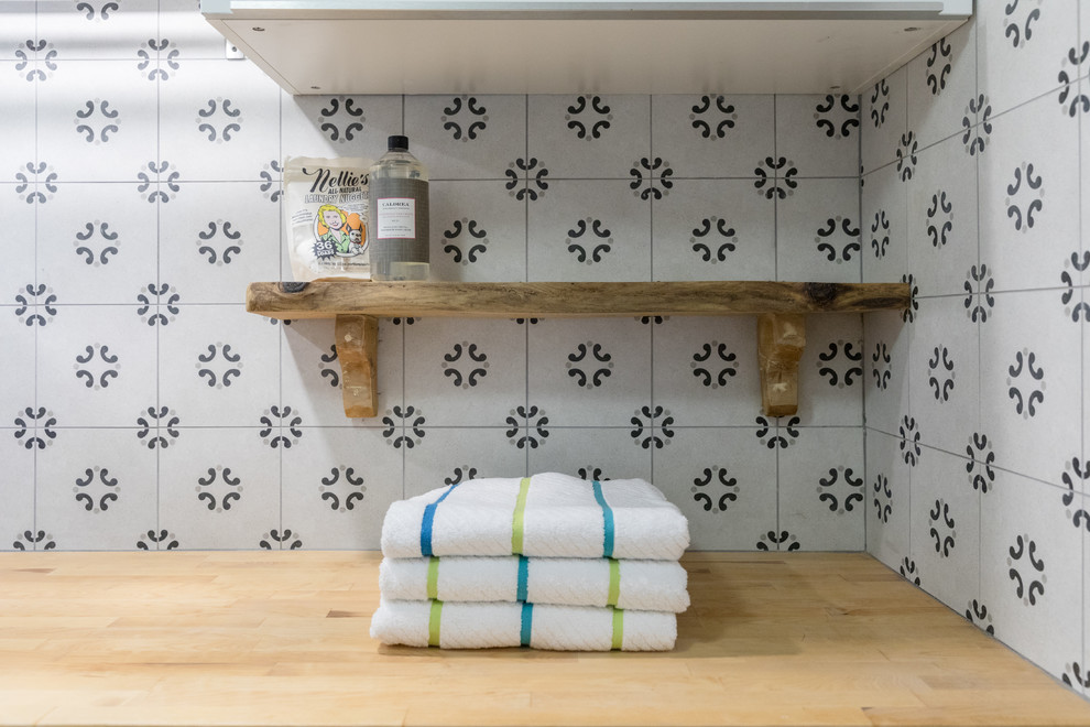 Imagen de cuarto de lavado lineal actual pequeño con armarios con paneles lisos, puertas de armario blancas, encimera de madera, paredes grises, suelo de madera clara y lavadora y secadora juntas