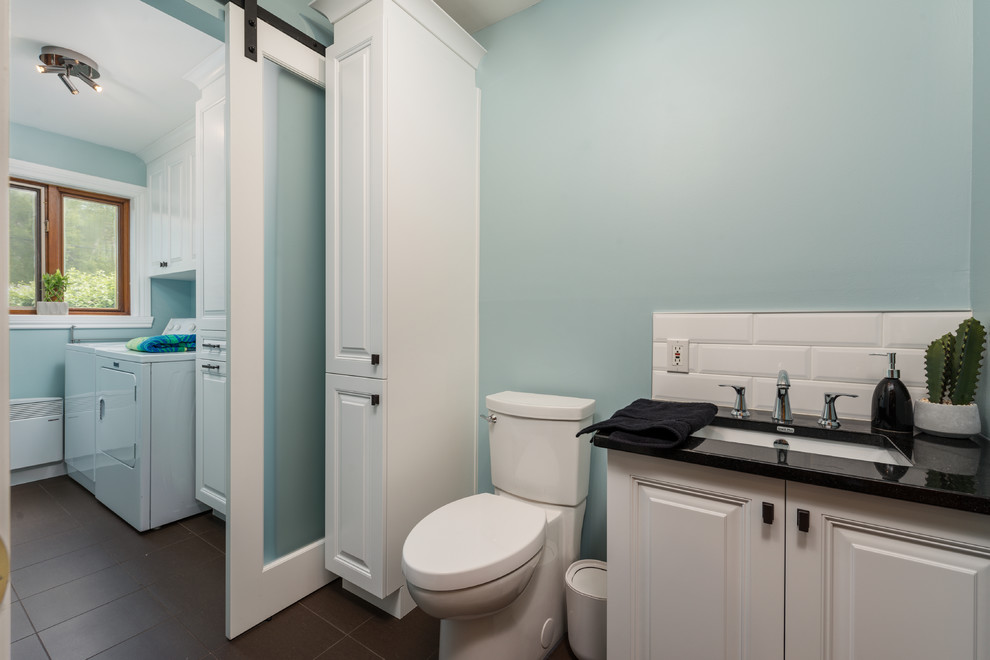Photo of a small classic single-wall utility room in Montreal with a submerged sink, raised-panel cabinets, white cabinets, granite worktops, blue walls, ceramic flooring, a side by side washer and dryer, brown floors and black worktops.