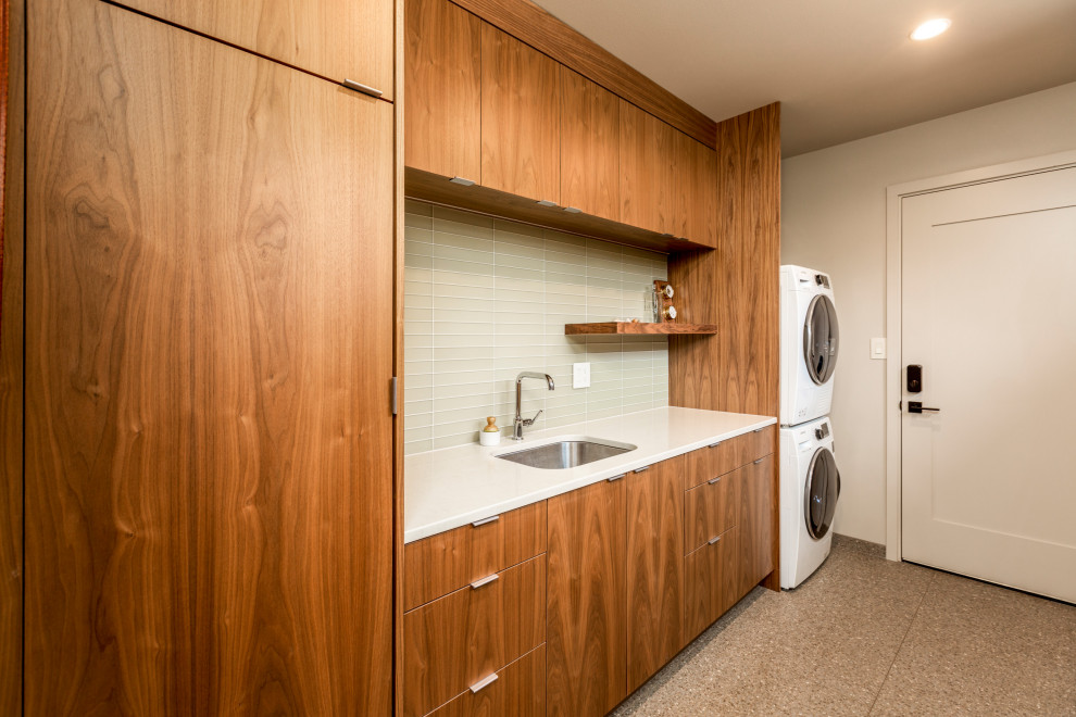 Foto på en stor retro vita parallell tvättstuga enbart för tvätt, med en undermonterad diskho, släta luckor, skåp i mellenmörkt trä, bänkskiva i kvarts, grönt stänkskydd, stänkskydd i glaskakel, vita väggar, kalkstensgolv, en tvättpelare och flerfärgat golv