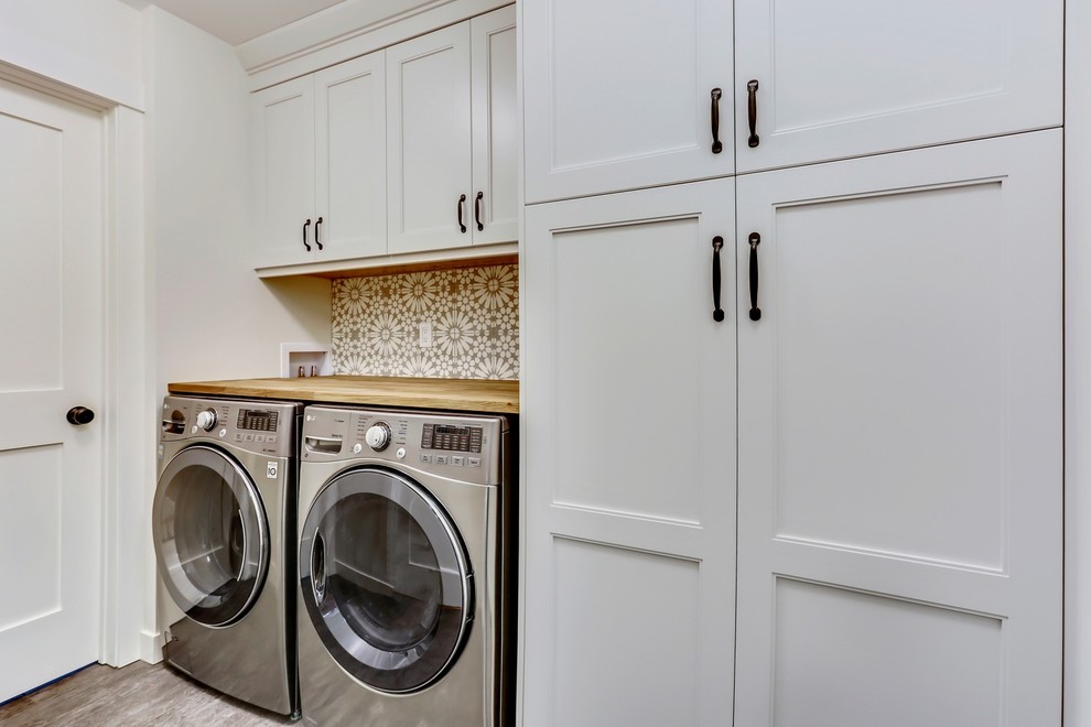 Immagine di una lavanderia multiuso tradizionale di medie dimensioni con ante in stile shaker, ante bianche, top in legno, pareti bianche, pavimento in vinile, lavatrice e asciugatrice affiancate e pavimento grigio