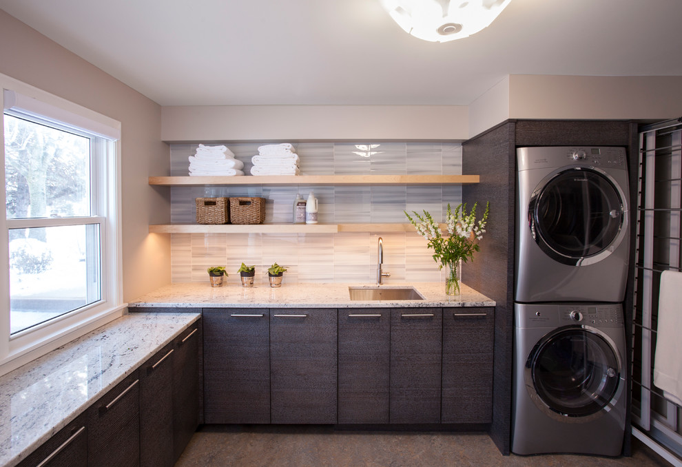 Example of a mid-sized minimalist l-shaped laminate floor and multicolored floor laundry room design in Minneapolis with an undermount sink, flat-panel cabinets, gray cabinets, granite countertops, beige walls and a stacked washer/dryer