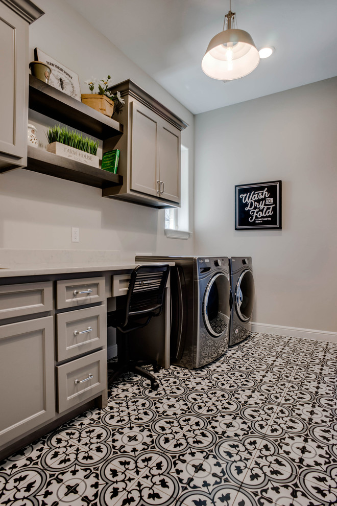 Lantlig inredning av en mellanstor vita vitt tvättstuga enbart för tvätt, med en undermonterad diskho, luckor med infälld panel, grå skåp, bänkskiva i kvarts, grå väggar, klinkergolv i keramik, en tvättmaskin och torktumlare bredvid varandra och flerfärgat golv