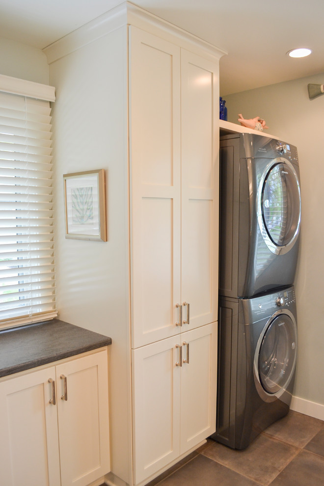 Ejemplo de lavadero clásico renovado de tamaño medio con armarios con paneles lisos, puertas de armario blancas, encimera de acrílico, suelo de baldosas de cerámica, lavadora y secadora apiladas, suelo gris y encimeras grises