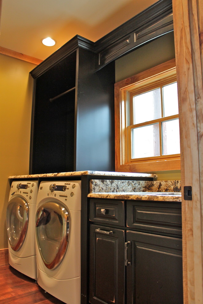 Foto di una sala lavanderia stile rurale di medie dimensioni con ante con bugna sagomata, ante nere, top in granito e lavatrice e asciugatrice affiancate
