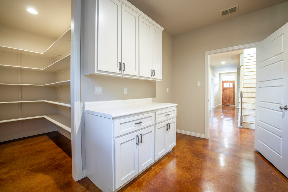 Large rustic l-shaped utility room in Austin with white cabinets, shaker cabinets, granite worktops, beige walls, concrete flooring, a stacked washer and dryer, brown floors and white worktops.