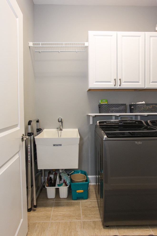 Example of a mid-sized transitional single-wall ceramic tile and beige floor dedicated laundry room design in Atlanta with an utility sink, raised-panel cabinets, white cabinets, gray walls and a side-by-side washer/dryer