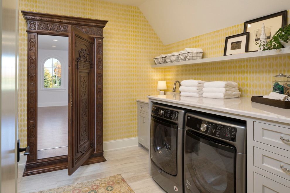 Inspiration för stora klassiska linjära tvättstugor enbart för tvätt, med luckor med infälld panel, grå skåp, gula väggar, en tvättmaskin och torktumlare bredvid varandra, beiget golv, marmorbänkskiva och ljust trägolv