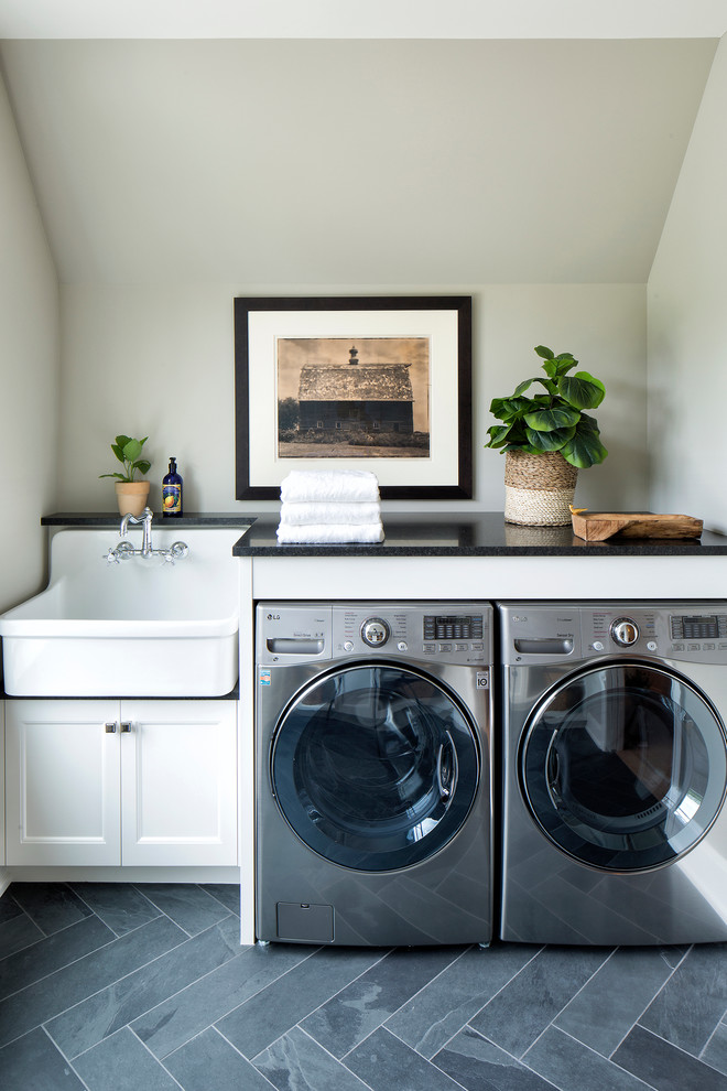Ejemplo de cuarto de lavado clásico renovado con armarios con paneles empotrados, puertas de armario blancas, lavadora y secadora juntas, fregadero sobremueble, suelo gris, encimeras negras y paredes grises