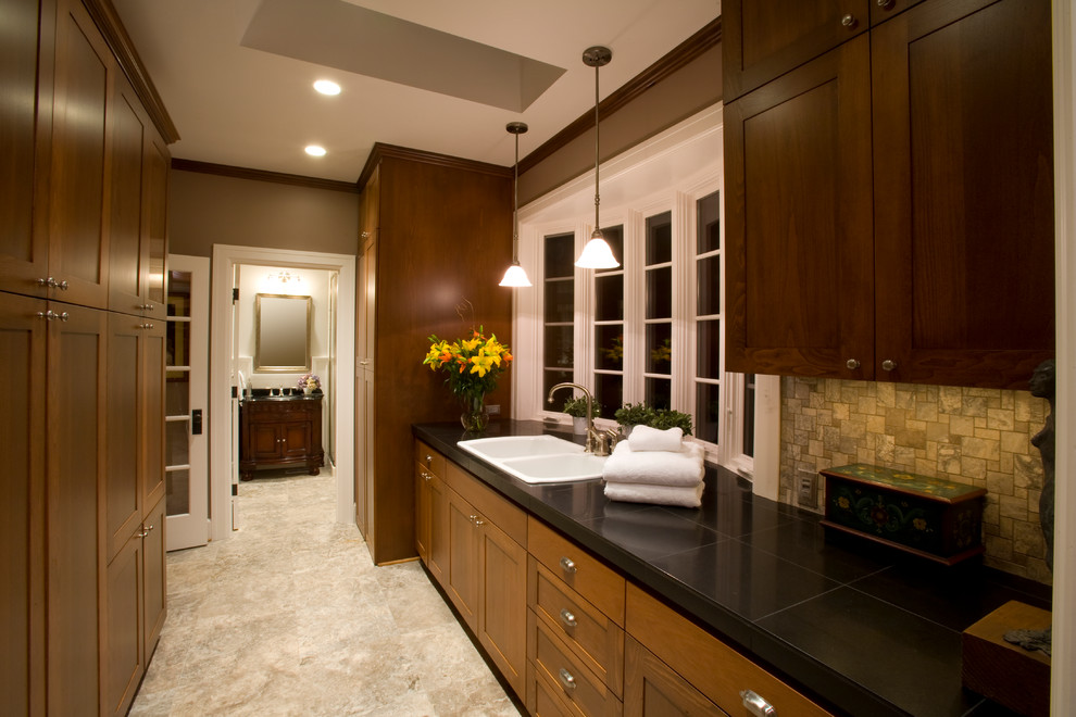 Large elegant galley travertine floor and beige floor dedicated laundry room photo in Portland with a double-bowl sink, shaker cabinets, medium tone wood cabinets, granite countertops, beige walls, a stacked washer/dryer and black countertops
