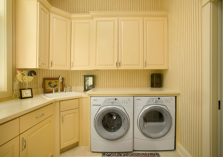 Foto di una grande lavanderia multiuso classica con lavello da incasso, ante con riquadro incassato, ante gialle, top in superficie solida, lavatrice e asciugatrice affiancate e pareti beige