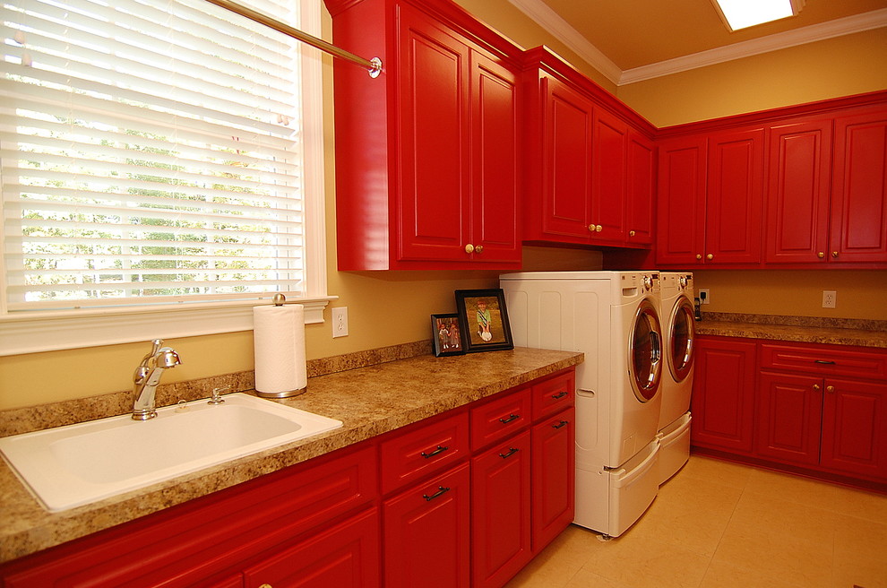 Exempel på en stor klassisk u-formad tvättstuga, med en nedsänkt diskho, luckor med upphöjd panel, röda skåp, laminatbänkskiva, bruna väggar, klinkergolv i keramik, en tvättmaskin och torktumlare bredvid varandra och beiget golv