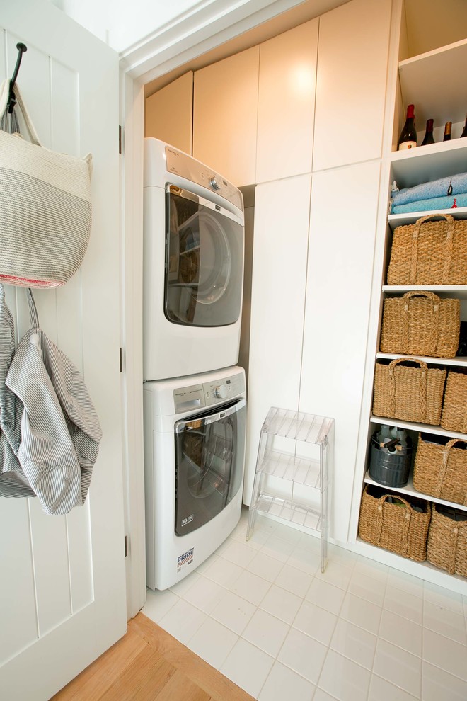 Imagen de armario lavadero lineal marinero pequeño con armarios con paneles lisos, puertas de armario blancas, suelo de baldosas de cerámica, lavadora y secadora apiladas y paredes blancas