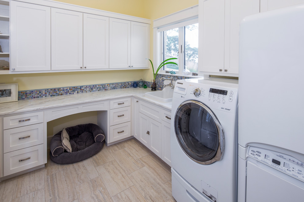 Idéer för stora amerikanska u-formade tvättstugor enbart för tvätt, med en rustik diskho, luckor med upphöjd panel, vita skåp, granitbänkskiva, gula väggar, klinkergolv i porslin och en tvättmaskin och torktumlare bredvid varandra